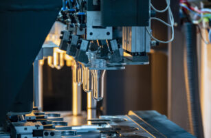 Close-up of an automated machine forming transparent plastic bottles, with robotic arms and mechanical components visible in an industrial setting.