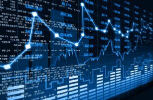 A digital screen displays fluctuating stock market charts with candlestick graphs, numerical data, and bar charts, all in shades of blue, representing financial analysis and trading activity.