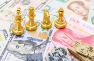 Gold chess pieces and toy tanks are placed on top of U.S. dollar and Chinese yuan banknotes, symbolising strategy, competition, and conflict between the United States and China.