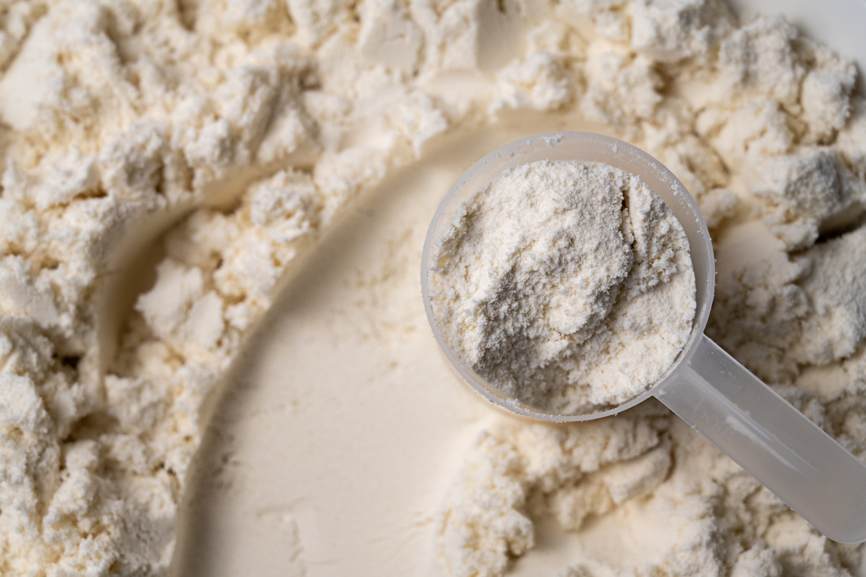 A close-up of a plastic scoop filled with a fine, off-white powder, resting on a larger pile of the same powder.