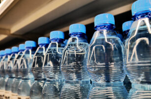 A row of clear plastic water bottles with blue caps lined up on a shelf.
