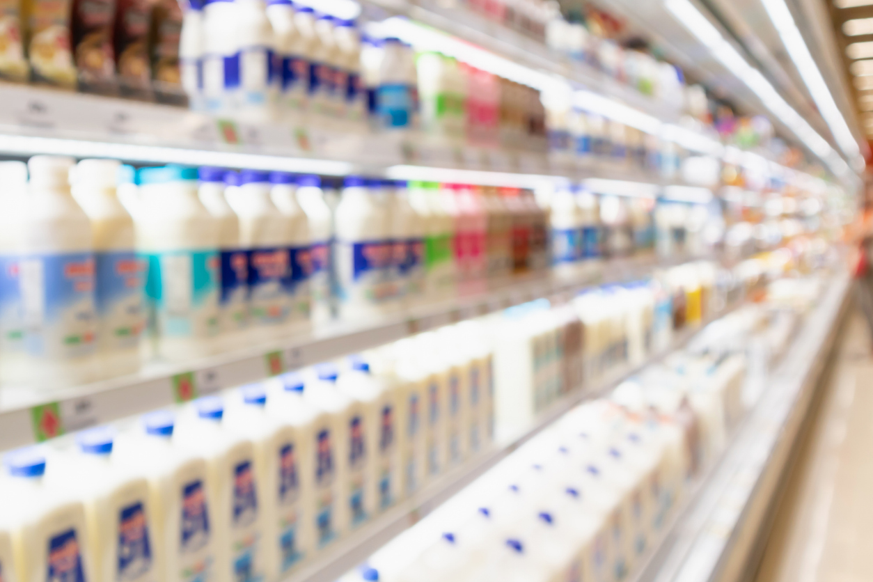 Blurred view of multiple shelves in a refrigerated supermarket aisle stocked with plastic bottles of milk.